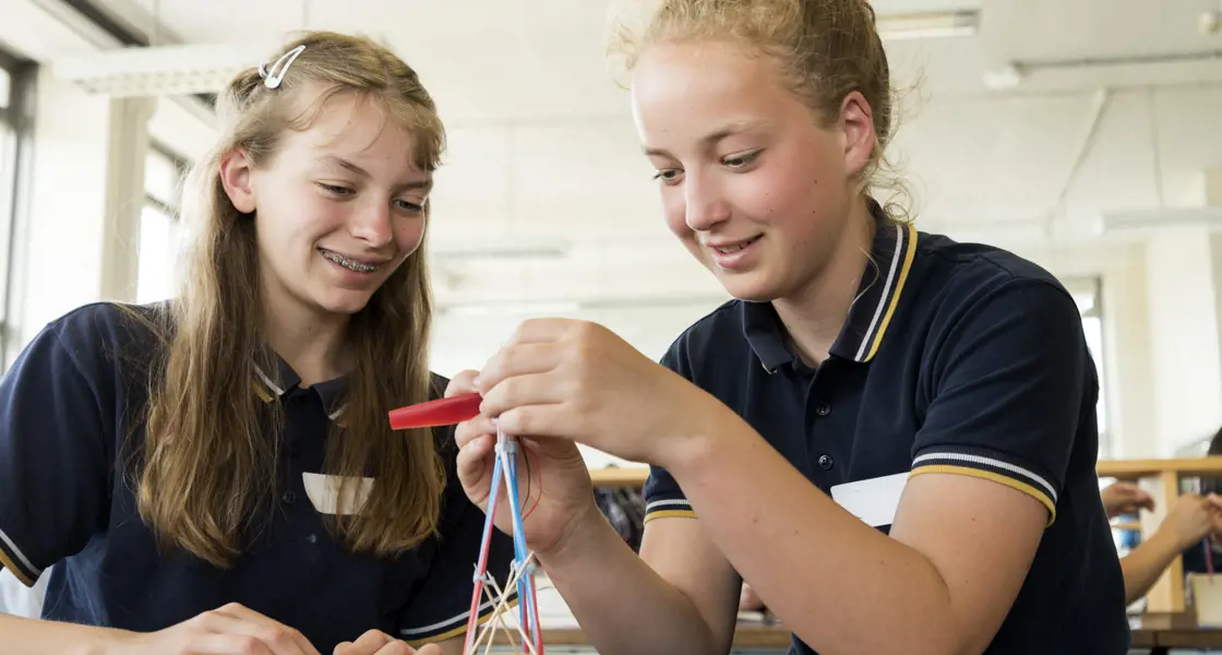 Two girls building a small tower shape project.