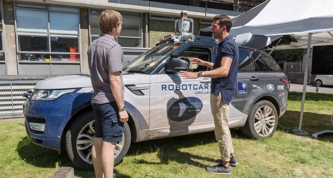 Two people outside talking next to a self-driving car